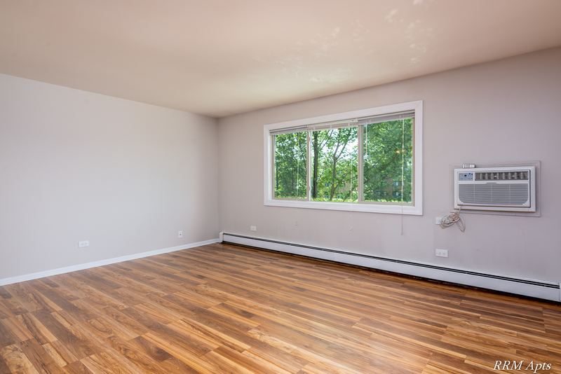 Living room with wood-look floor, window with trees and a wall air conditioner, Pioneer Court apartment 900 3A