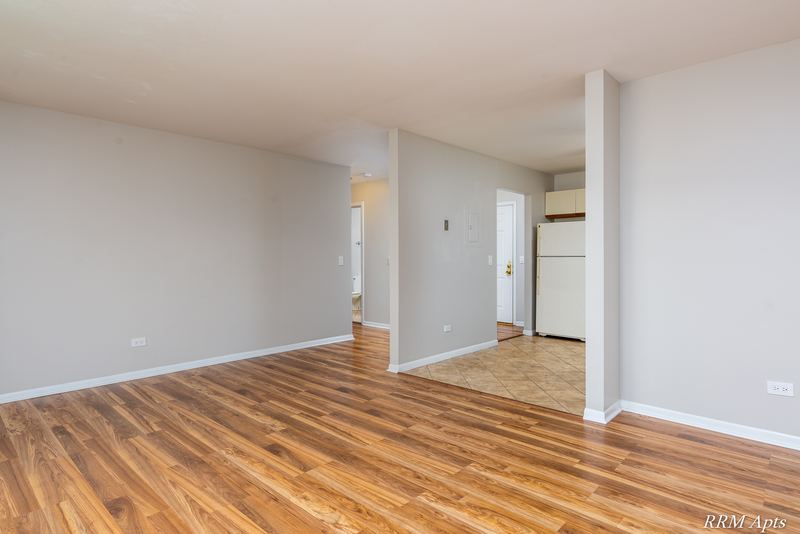 Living room with wood-look floor, a half wall and a hallway to the tile-floored kitchen, Pioneer Court apartment 900 3A