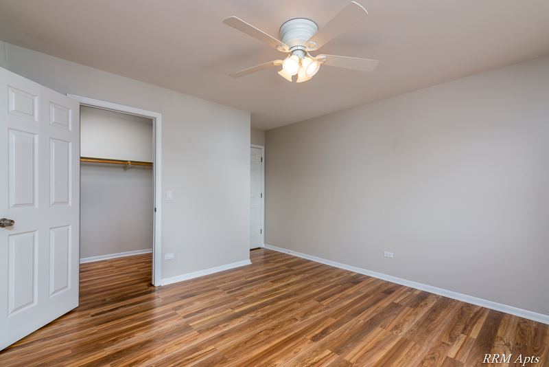 Bedroom with wood-look floor, ceiling fan, white door and an open closet with a shelf, Pioneer Court apartment 900 3A