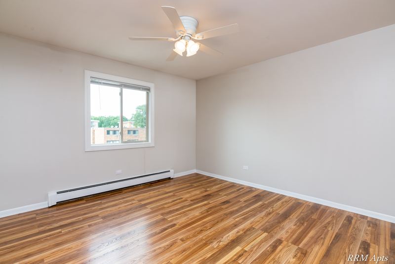 Bedroom with wood-look floor, ceiling fan, window with rooftop view and a baseboard heater, Pioneer Court apartment 900 3A