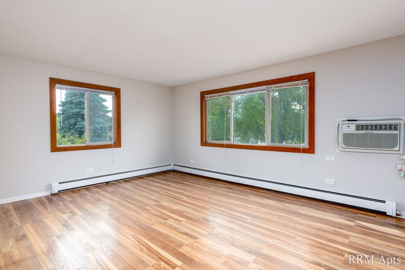 Living room with wood-look floor, two oak-trimmed windows with trees and a baseboard heater, Pioneer Court apartment 900 3C