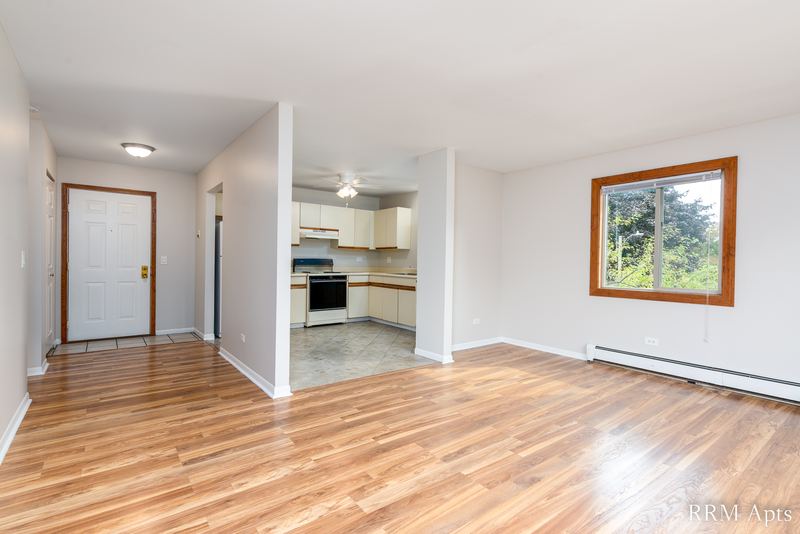 Living room with wood-look floor, white entry door, half wall and a window with trees, Pioneer Court apartment 900 3C