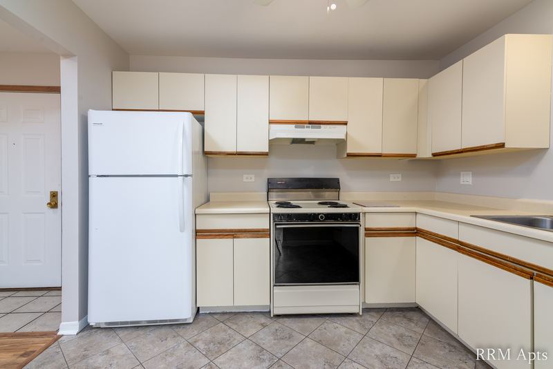 Kitchen with white oak-trimmed cabinets, white refrigerator, black stove and tile floor, Pioneer Court apartment 900 3C