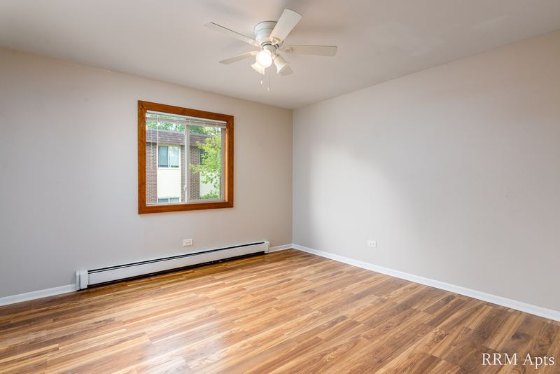 Bedroom with wood-look floor, ceiling fan, gray walls and an oak-trimmed window with trees, Pioneer Court apartment 900 3C