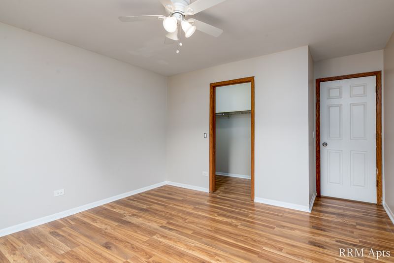 Bedroom with wood-look floor, ceiling fan, open closet and a white door, Pioneer Court apartment 900 3C