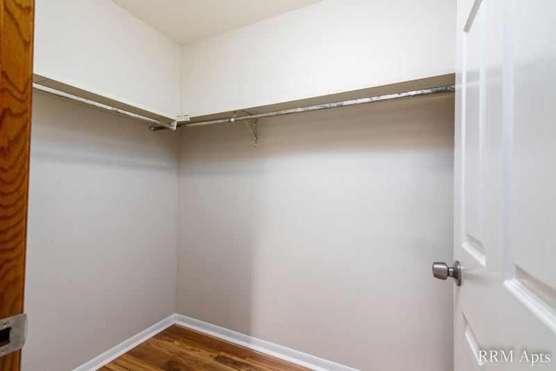 Closet with wood-look floor, long shelf with a hanging rod and a white door, Pioneer Court apartment 900 3C