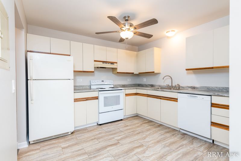 Kitchen with white oak-trimmed cabinets, white appliances, ceiling fan and wood-look floor, Pioneer Court apartment 900-3D