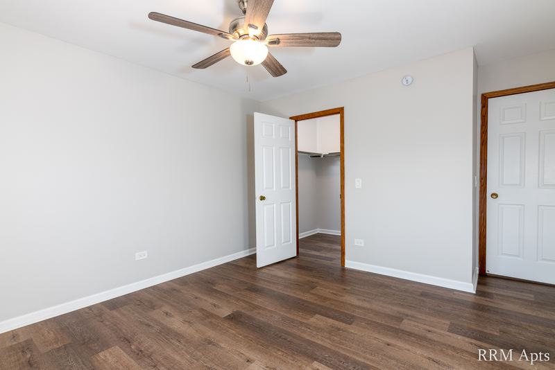 Bedroom with wood-look floor, ceiling fan, open closet door and a white door, Pioneer Court apartment 900-3D