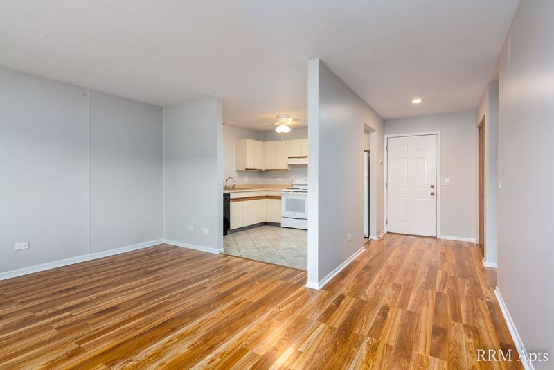 Living room with wood-look floor, half wall, white entry door and a view into the kitchen, Pioneer Court apartment 918 1B