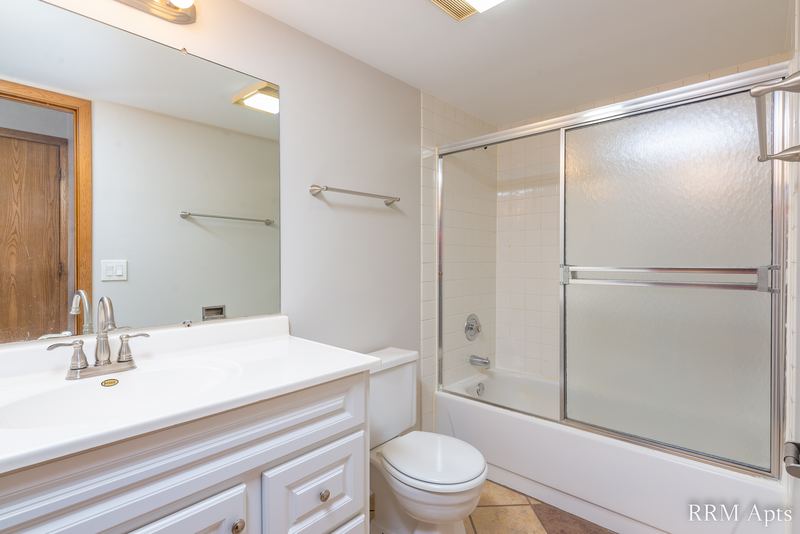 Bathroom with white vanity, wide mirror, sliding glass tub doors and toilet, Pioneer Court apartment 918 1B