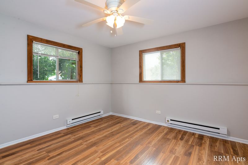 Bedroom with wood-look floor, ceiling fan, two windows with trees and baseboard heaters, Pioneer Court apartment 918 1B