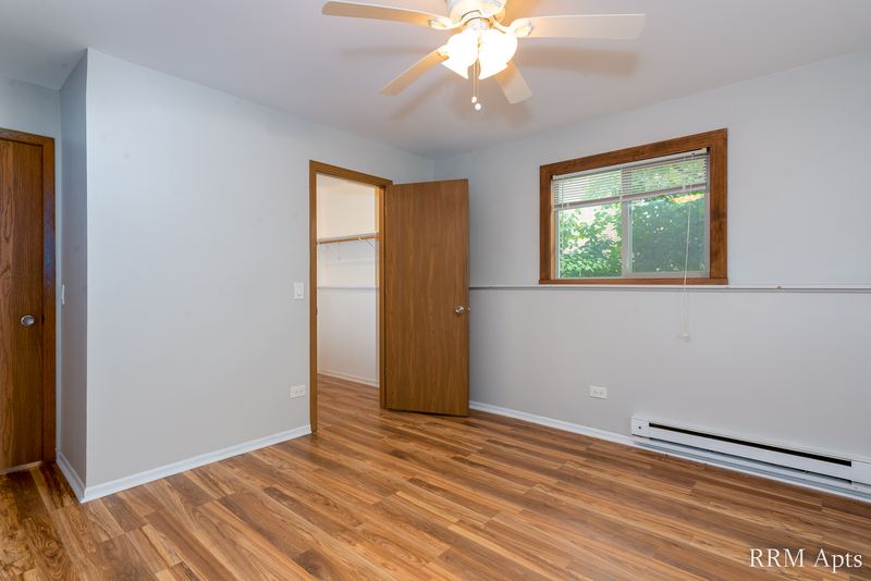 Bedroom with wood-look floor, ceiling fan, open closet, oak door and a window with trees, Pioneer Court apartment 918 1B