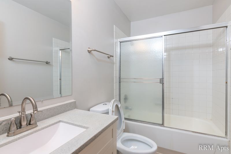 Bathroom with white vanity and mirror, toilet and a tub with sliding glass doors, Pioneer Court apartment 918-1E