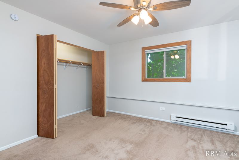 Bedroom with beige carpet, ceiling fan, window and an open closet with wood folding doors, Pioneer Court apartment 918-1E