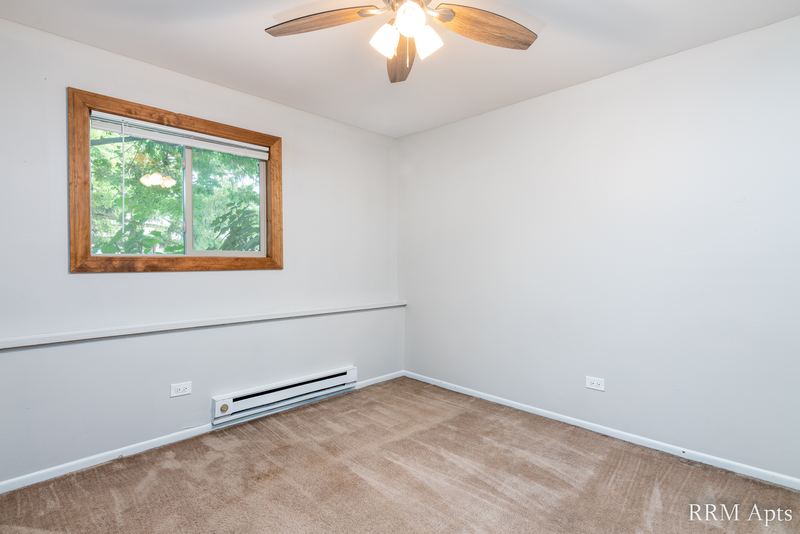 Empty room with beige carpet, one wood-trimmed window, ceiling fan and baseboard heater, Pioneer Court apartment 918-1E