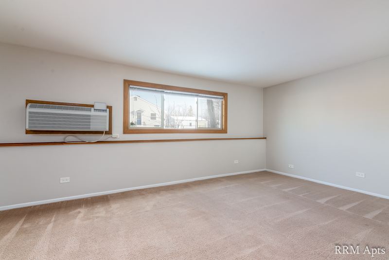 Living room with beige carpet, wall air conditioner, window with wood trim and a chair rail, Pioneer Court apartment 918-1F