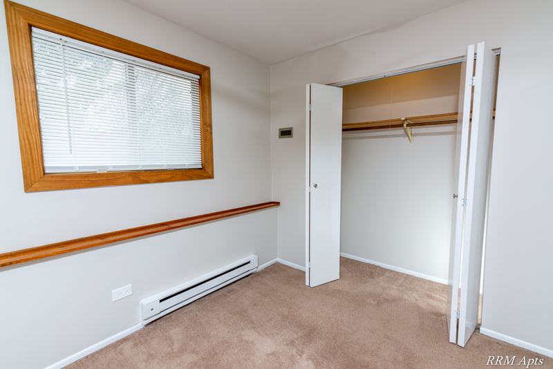 Bedroom with beige carpet, wide window with blinds and open white folding closet doors, Pioneer Court apartment 918-1F