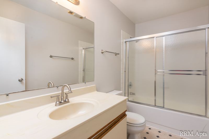 Bathroom with cream vanity and mirror, toilet and a tub with sliding glass doors, Pioneer Court apartment 918-1F