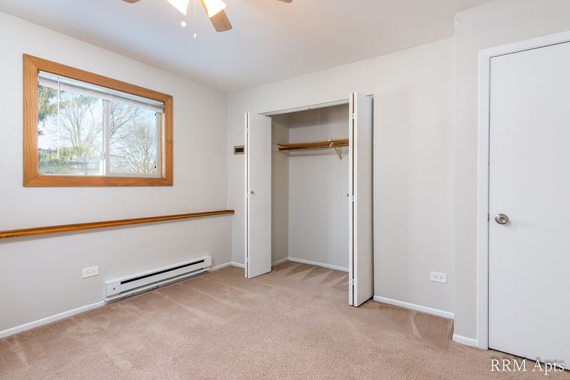 Bedroom with beige carpet, window, open closet with white folding doors and a doorway, Pioneer Court apartment 918-1F