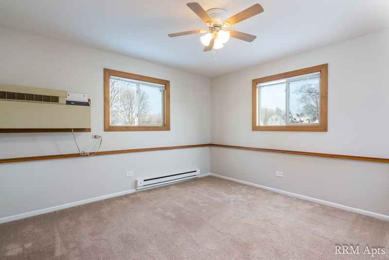 Living room with beige carpet, two windows, wall air conditioner, chair rail and ceiling fan, Pioneer Court apartment 918-1F