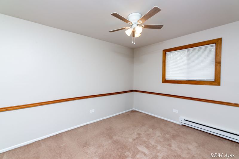 Empty room with beige carpet, wood-trimmed window in the corner, chair rail and ceiling fan, Pioneer Court apartment 918-1F