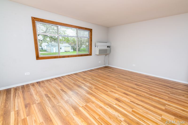 Living room with wood floor, wide wood-trimmed window and a wall air conditioner, Pioneer Court apartment 918-2D