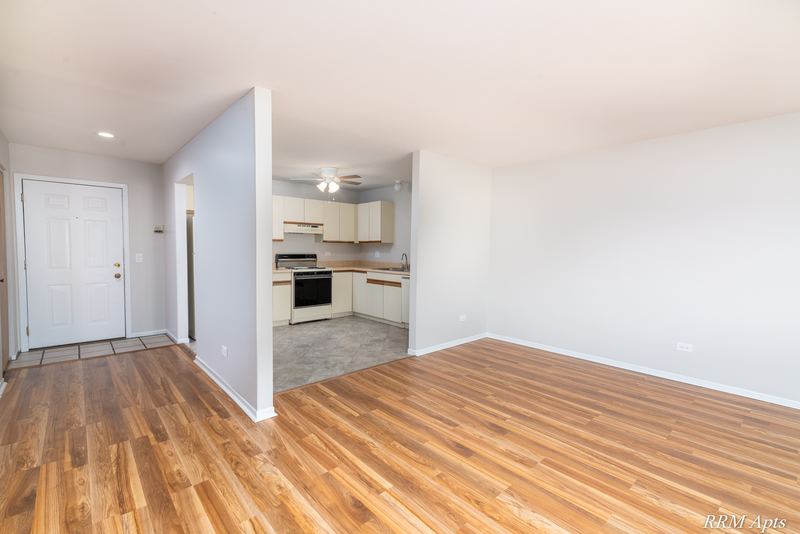 Living room with wood floor, entry door and an opening to the kitchen, Pioneer Court apartment 918-2D