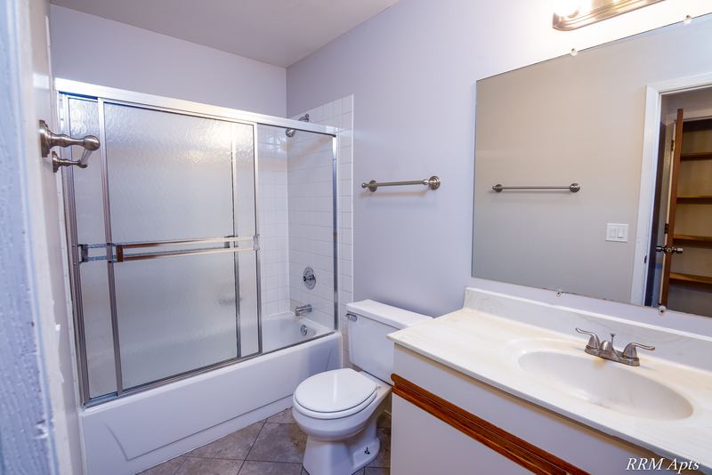 Bathroom with tub with sliding glass doors, toilet and a cream vanity, Pioneer Court apartment 918-2D