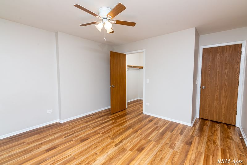 Empty room with wood floor, ceiling fan and two wood doors, one open to a hallway, Pioneer Court apartment 918-2D