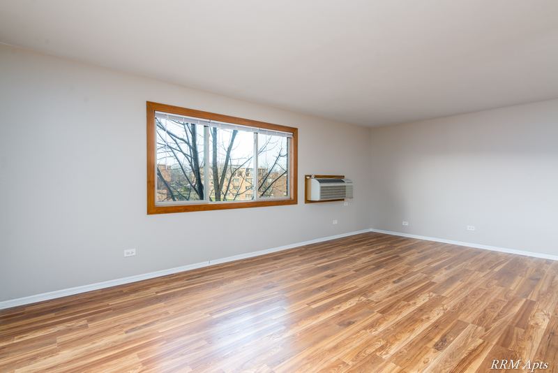 Living room with wood-look floor, oak-trimmed window and a wall air conditioner, Pioneer Court apartment 918 2E