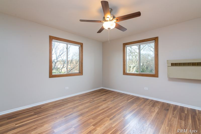 Bedroom with wood-look floor, ceiling fan, two windows and a wall air conditioner, Pioneer Court apartment 918 2E