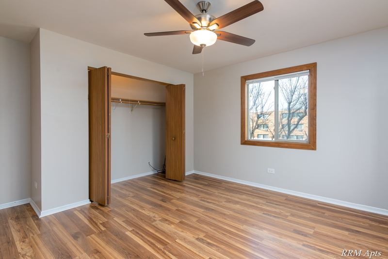 Bedroom with wood-look floor, ceiling fan, open oak closet doors and a window with trees, Pioneer Court apartment 918 2E