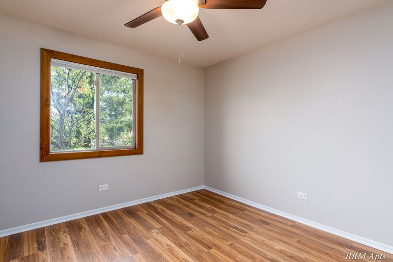 Bedroom with wood-look floor, ceiling fan and an oak-trimmed window with trees outside, Pioneer Court apartment 918 2E