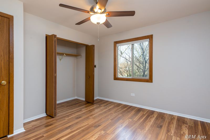 Bedroom with wood-look floor, ceiling fan, oak door, open closet and a window with trees, Pioneer Court apartment 918 2E