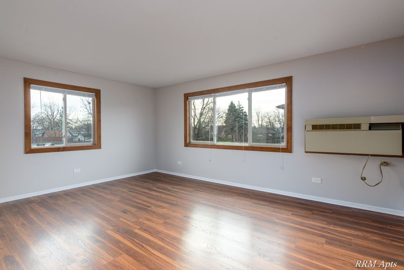 Living room with wood-look floor, two oak-trimmed windows and a wall air conditioner, Pioneer Court apartment 918 3A