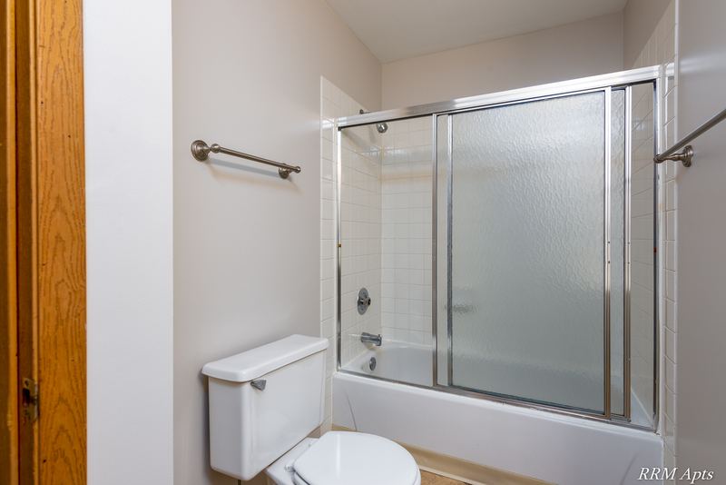 Bathroom with sliding glass tub doors, toilet, towel bar and an oak door, Pioneer Court apartment 918 3A