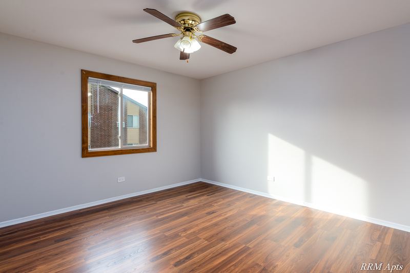 Bedroom with wood-look floor, ceiling fan and an oak-trimmed window facing a brick wall, Pioneer Court apartment 918 3A