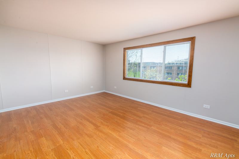 Empty room with wood floor and a wide wood-trimmed window with a building outside, Pioneer Court apartment 918-3C