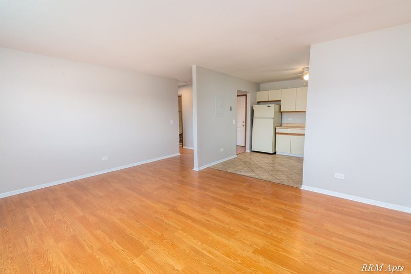 Living room with wood floor, ceiling fan and an opening to the kitchen and hall, Pioneer Court apartment 918-3C