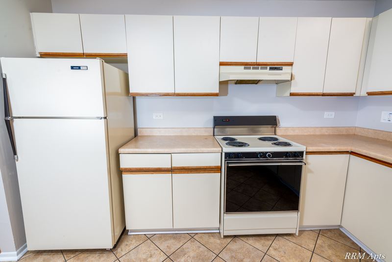 Kitchen corner with white refrigerator, electric stove under a range hood and white cabinets, Pioneer Court apartment 918-3C