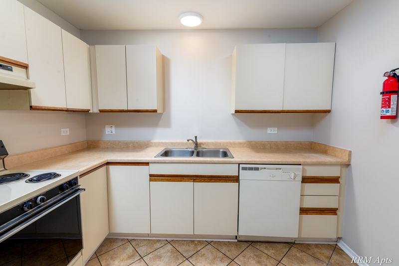 Kitchen with white cabinets, double sink, white dishwasher and a wall fire extinguisher, Pioneer Court apartment 918-3C
