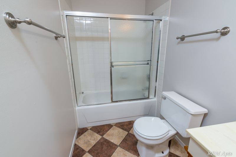 Bathroom with tub with sliding glass doors, toilet and a checkered tile floor, Pioneer Court apartment 918-3C