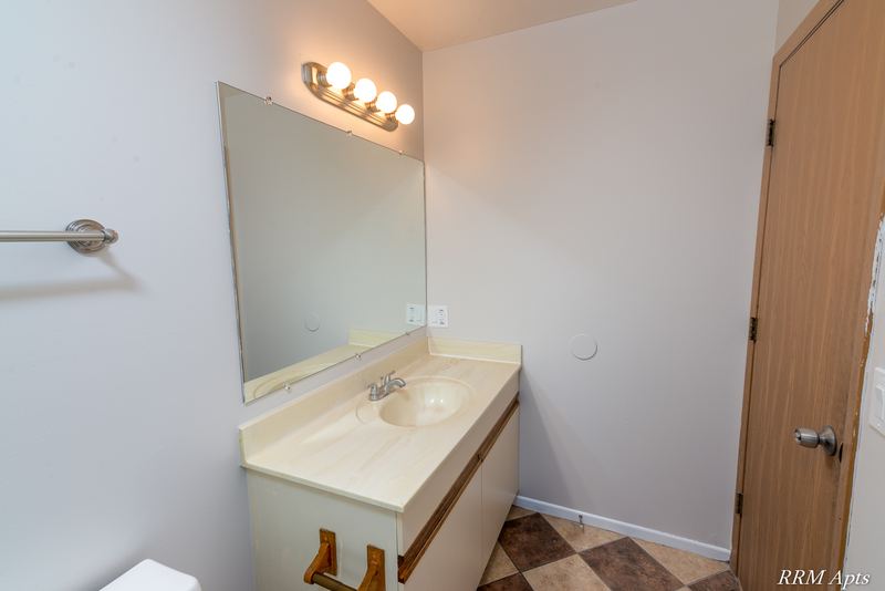 Bathroom with cream vanity, mirror with light bar, wood door and tile floor, Pioneer Court apartment 918-3C
