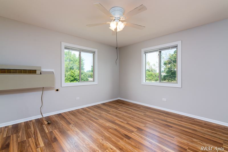 Empty room with wood floor, two windows onto trees, ceiling fan and a wall air conditioner, Pioneer Court apartment 918 3F