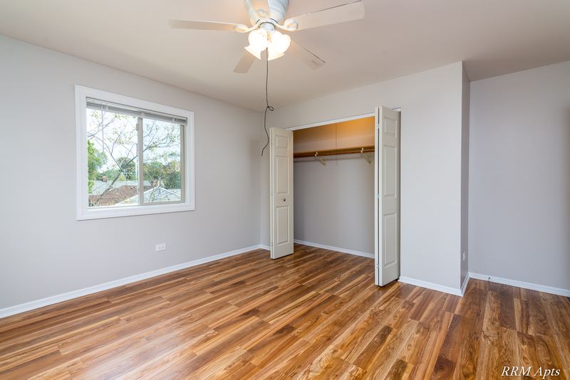Bedroom with wood floor, window, ceiling fan and an open closet with folding doors, Pioneer Court apartment 918 3F