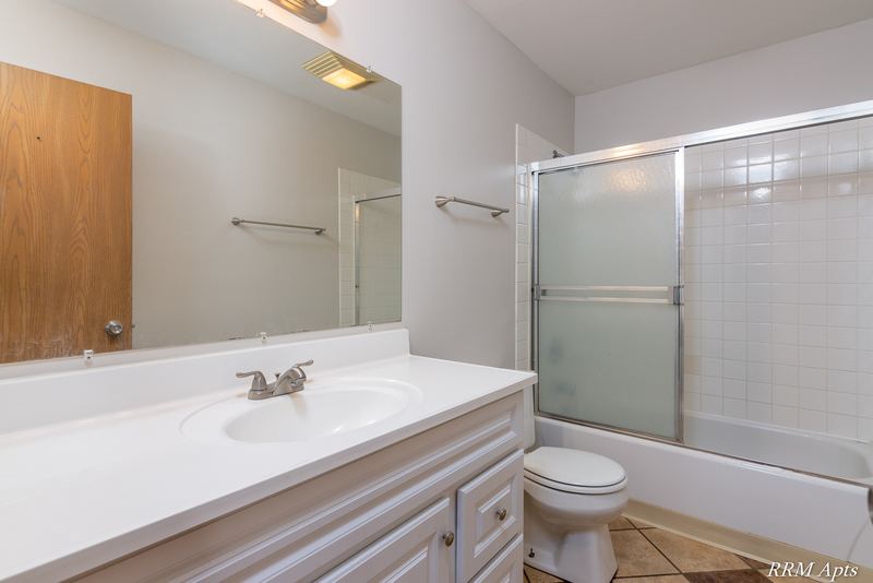 Bathroom with oak-trimmed white vanity, mirror, sliding glass tub doors and toilet, Pioneer Court apartment 918 3F