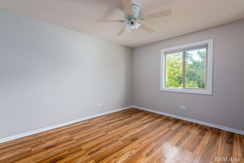 Bedroom with wood-look floor, ceiling fan, oak-trimmed window with trees and gray walls, Pioneer Court apartment 918 3F