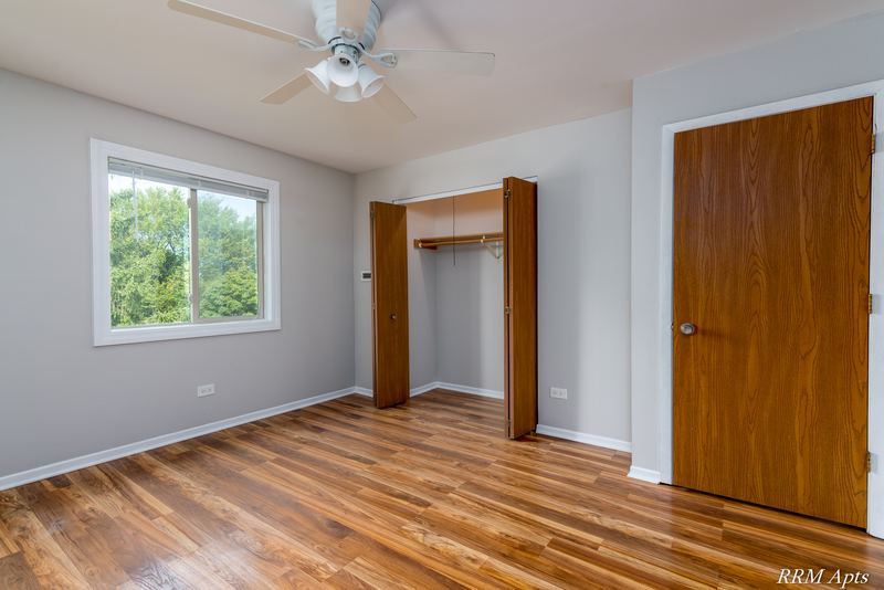 Bedroom with wood-look floor, ceiling fan, open closet, window with trees and an oak door, Pioneer Court apartment 918 3F