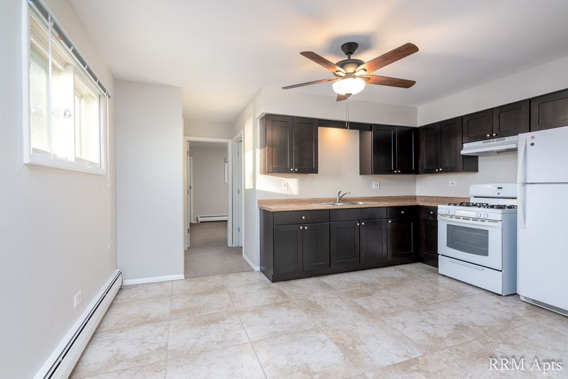 Kitchen with dark brown cabinets, white stove and refrigerator, ceiling fan and tile floor, Pistakee Road apartment 1A