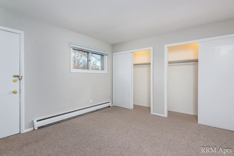 Bedroom with beige carpet, window, two open closets and baseboard heater, Pistakee Road apartment 1A